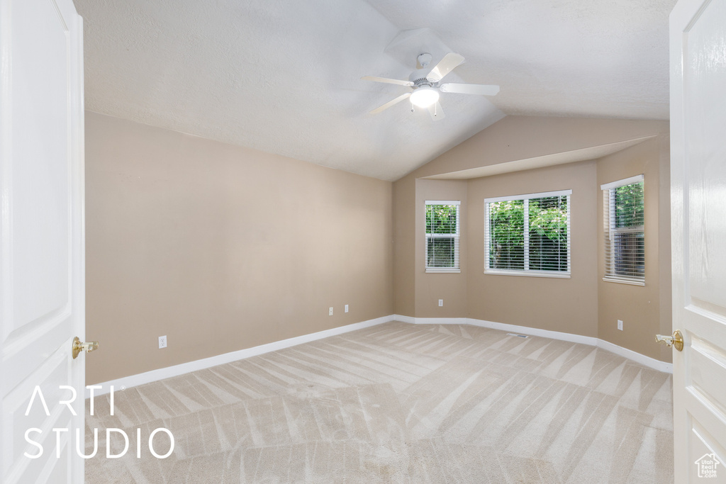 Spare room featuring light colored carpet, lofted ceiling, and ceiling fan