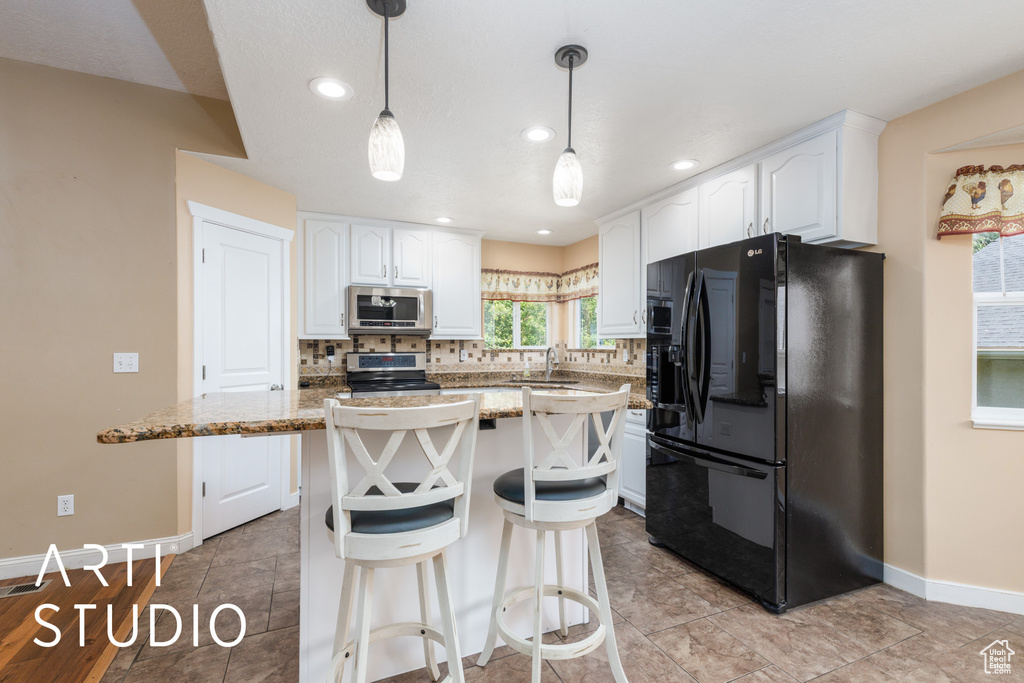 Kitchen with stainless steel appliances, white cabinets, backsplash, a center island, and decorative light fixtures