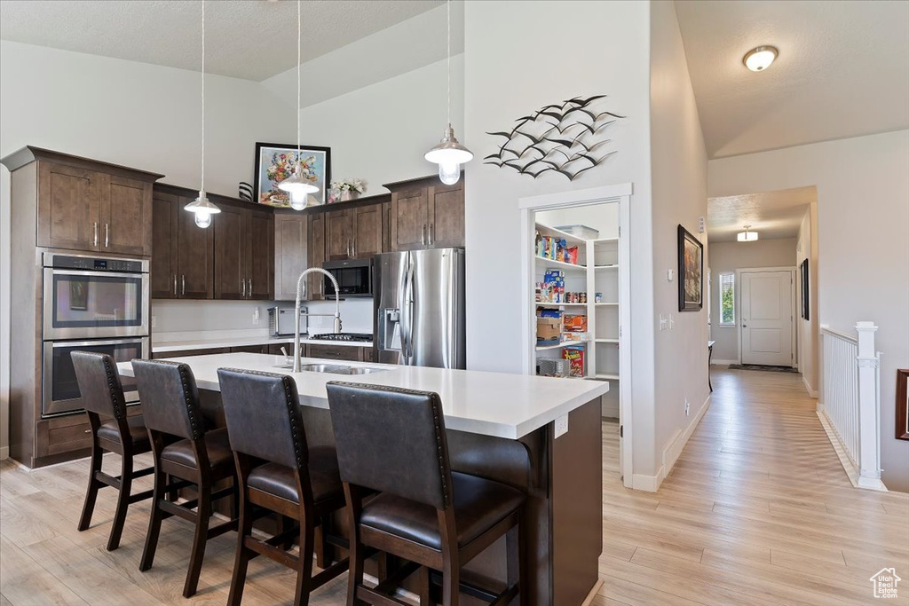 Kitchen with stainless steel appliances, dark brown cabinets, light countertops, light wood finished floors, and a breakfast bar
