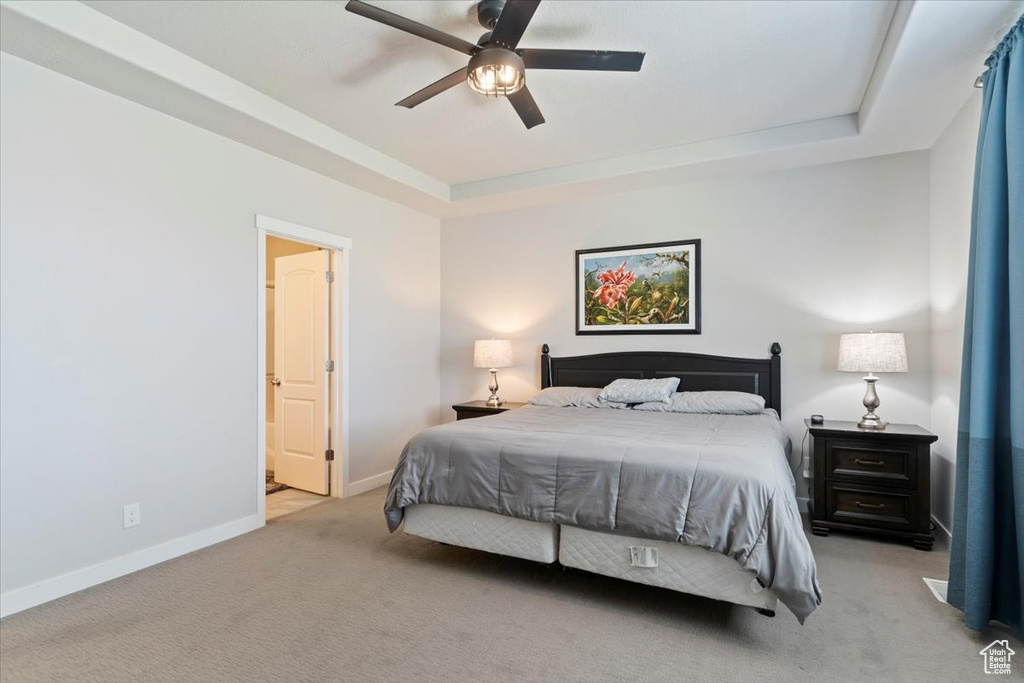 Carpeted bedroom with a tray ceiling and a ceiling fan