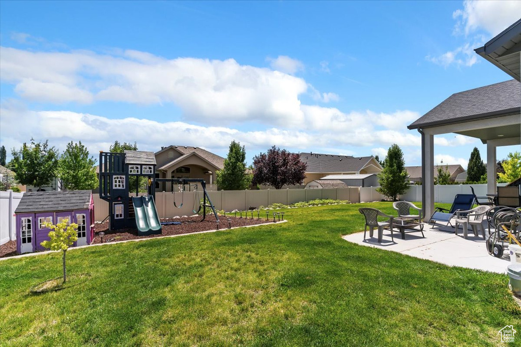 Fenced backyard with a patio, a playground, and an outbuilding