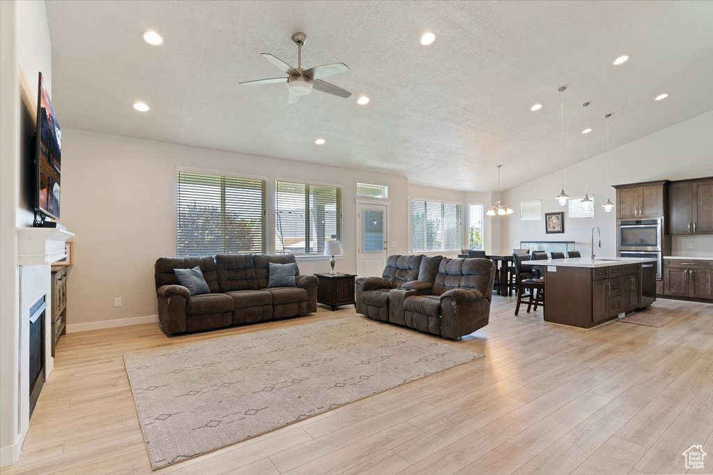 Living room with ceiling fan, light wood finished floors, recessed lighting, a fireplace, and a chandelier