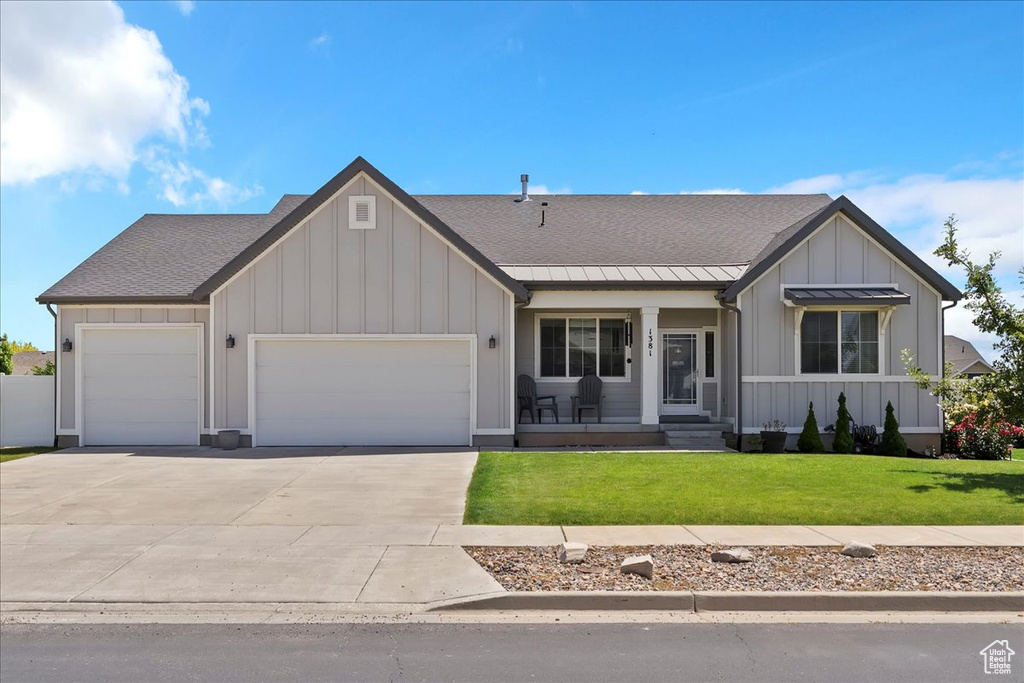 View of front of property with board and batten siding, an attached garage, a front yard, driveway, and covered porch
