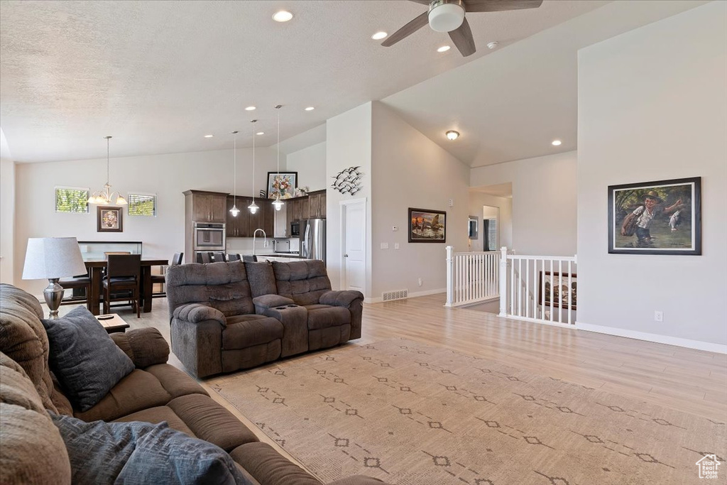 Living area featuring light wood-style floors, a chandelier, a ceiling fan, recessed lighting, and high vaulted ceiling