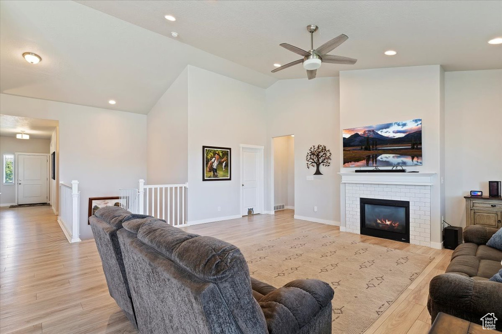 Living area with light wood-type flooring, a ceiling fan, a brick fireplace, high vaulted ceiling, and recessed lighting