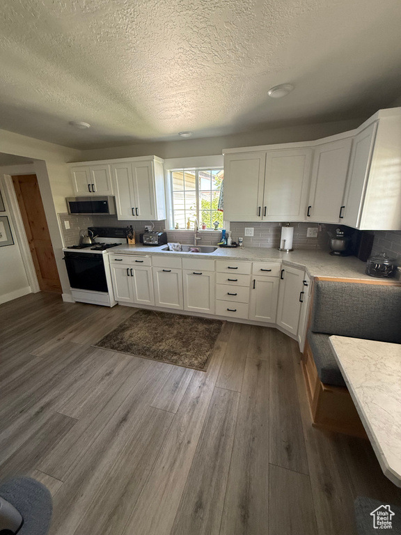 Kitchen with white range oven, stainless steel microwave, a textured ceiling, dark wood-style flooring, and white cabinets