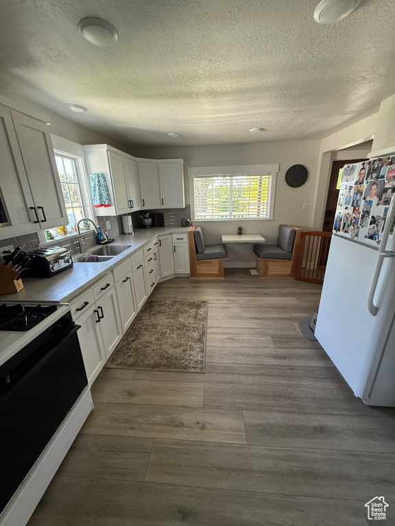 Kitchen featuring black range oven, freestanding refrigerator, a textured ceiling, plenty of natural light, and white cabinetry