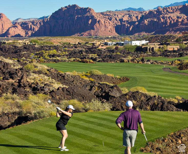 View of home's community with view of golf course, a mountain view, and a yard