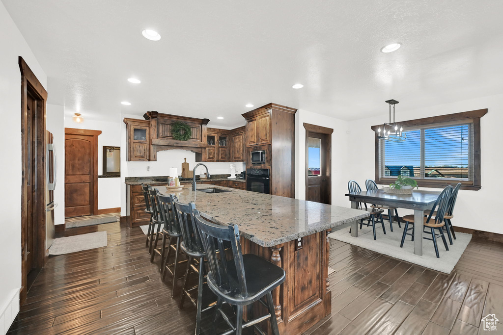 Kitchen with light stone countertops, sink, an island with sink, decorative light fixtures, and black oven