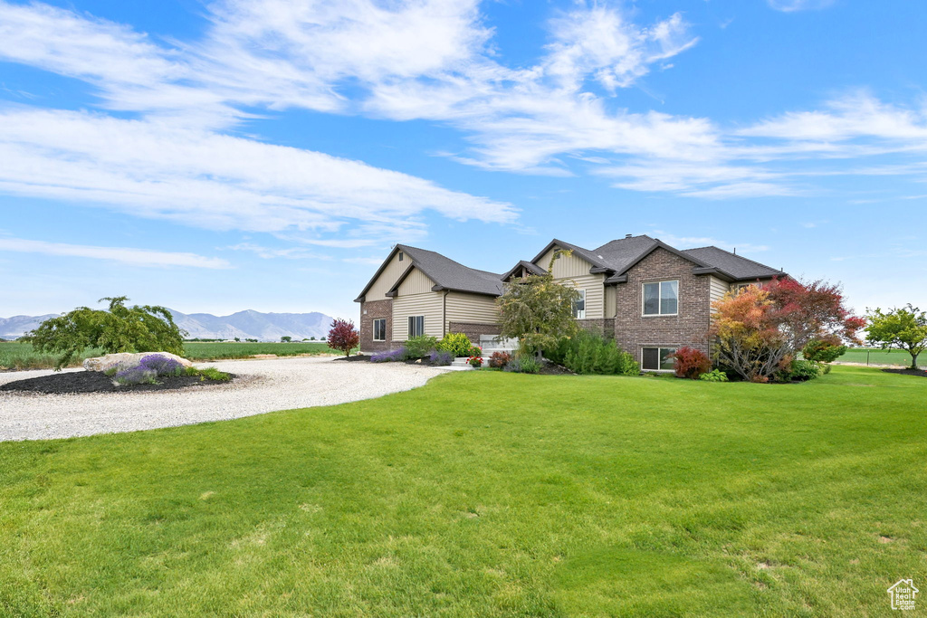 View of front of property featuring a mountain view, a front yard, gravel driveway, and brick siding