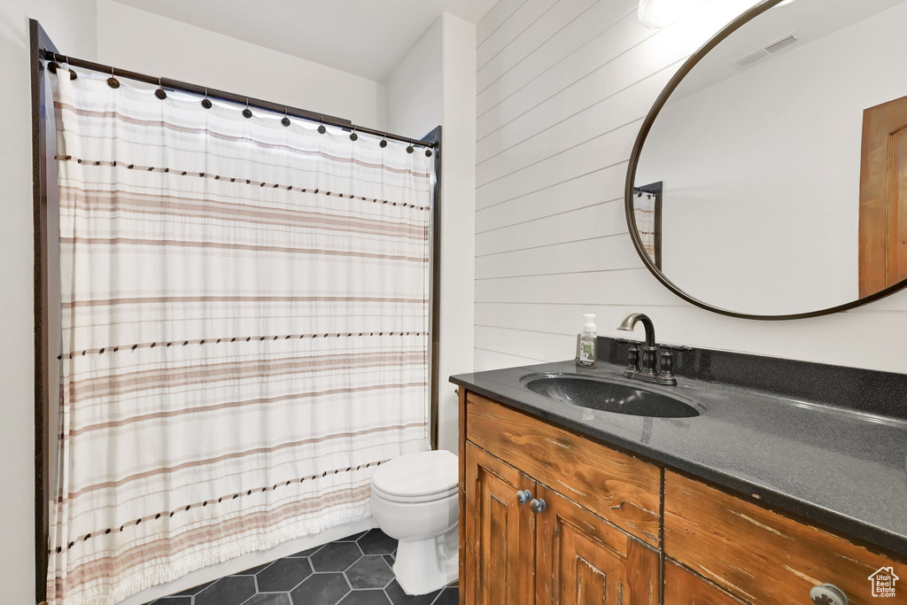 Bathroom with tile patterned floors, vanity, toilet, and wooden walls