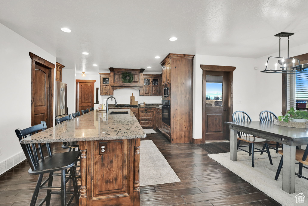 Kitchen with stainless steel appliances, sink, pendant lighting, dark hardwood / wood-style floors, and an island with sink
