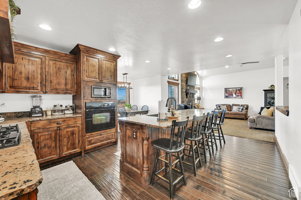Kitchen featuring a breakfast bar, sink, a center island with sink, black oven, and stainless steel microwave
