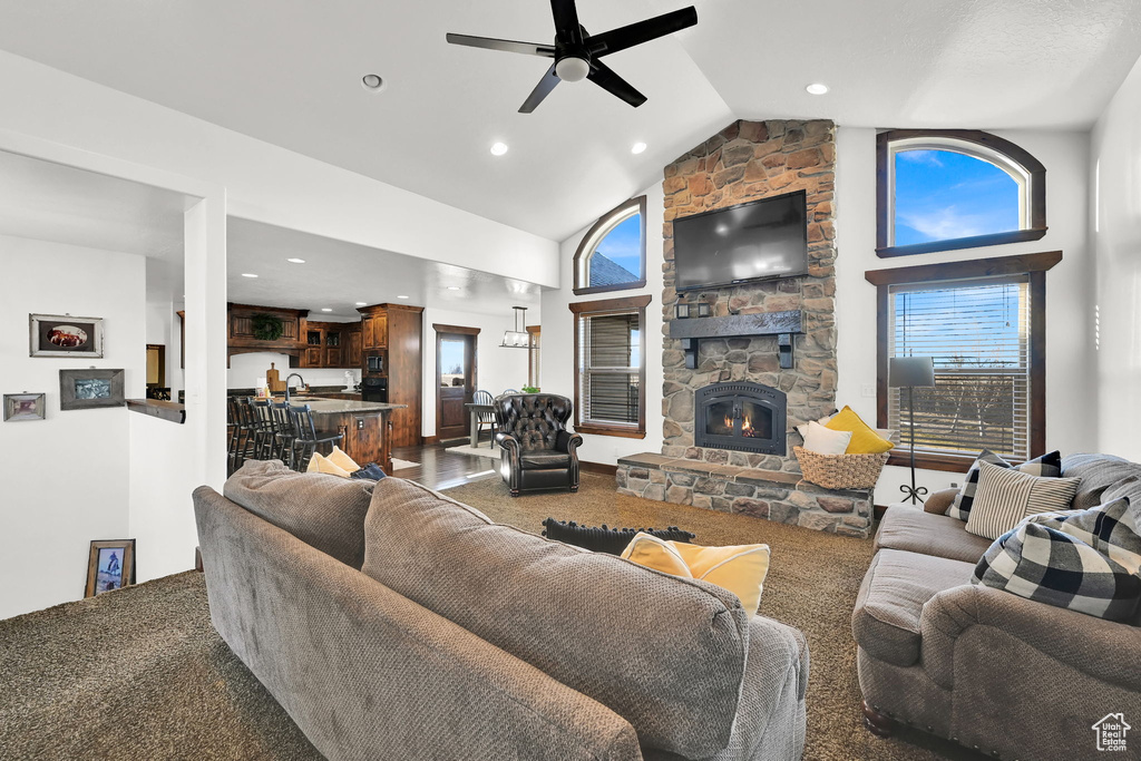 Carpeted living room featuring high vaulted ceiling, a stone fireplace, and ceiling fan