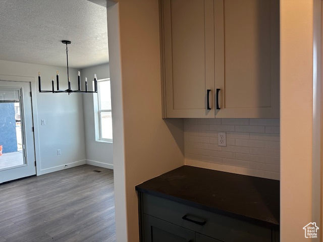 Kitchen with dark countertops, a chandelier, tasteful backsplash, a textured ceiling, and wood finished floors