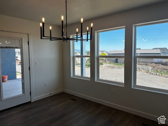 Unfurnished dining area featuring a chandelier, dark wood finished floors, and a textured ceiling