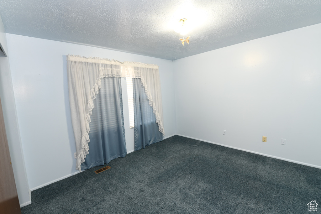 Spare room with dark carpet and a textured ceiling