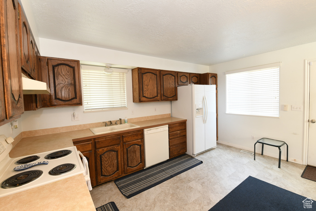 Kitchen with white appliances, under cabinet range hood, light countertops, and light floors