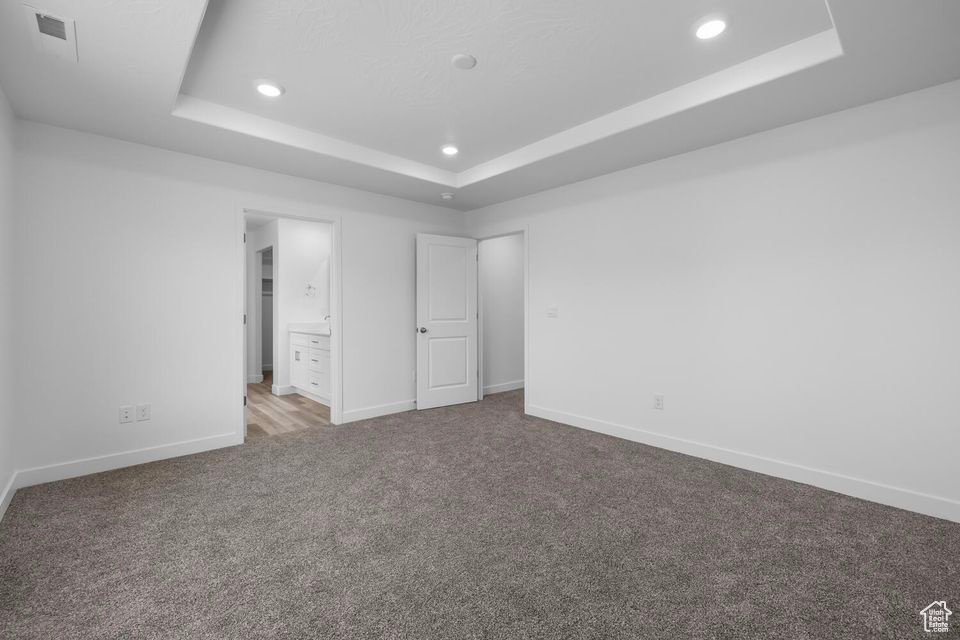 Unfurnished bedroom featuring a raised ceiling, carpet flooring, recessed lighting, and connected bathroom