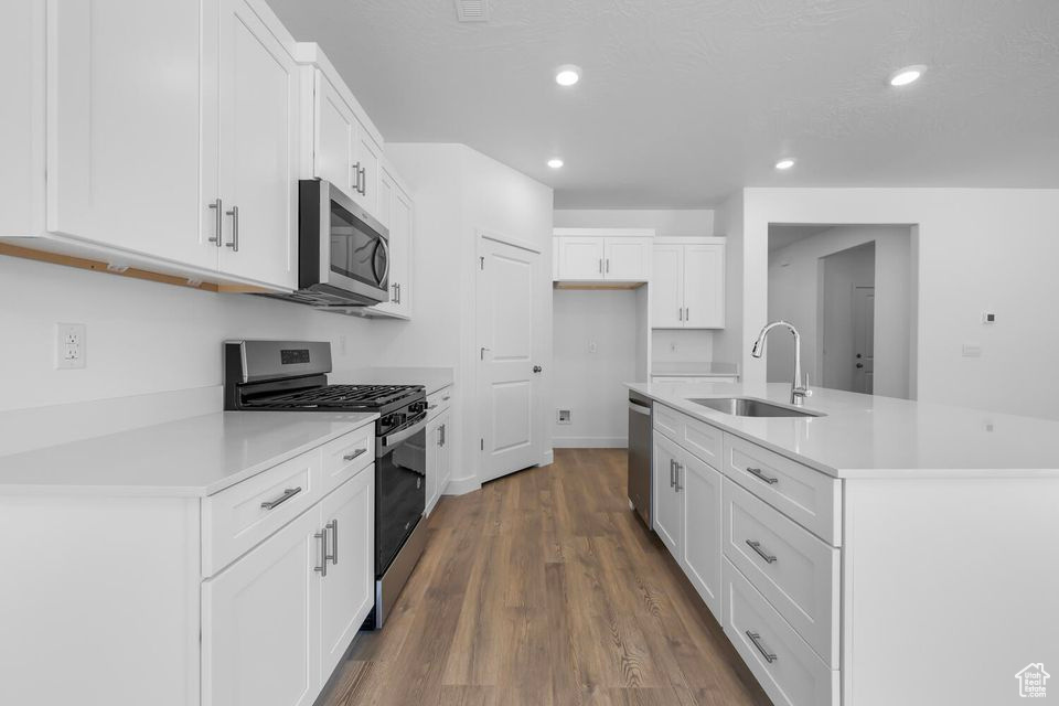 Kitchen featuring stainless steel appliances, wood finished floors, white cabinetry, recessed lighting, and light countertops