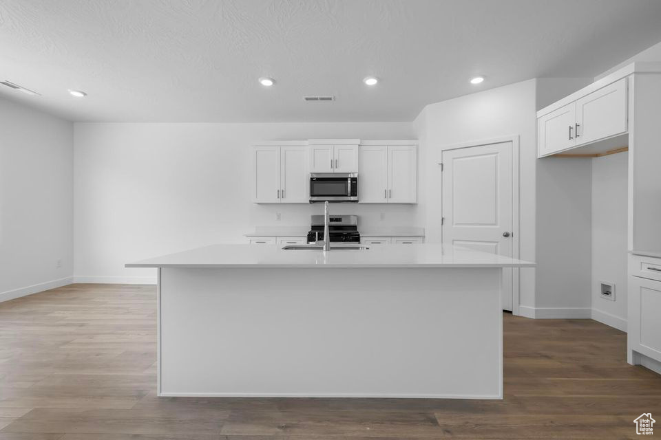 Kitchen featuring stainless steel microwave, light countertops, an island with sink, white cabinets, and recessed lighting