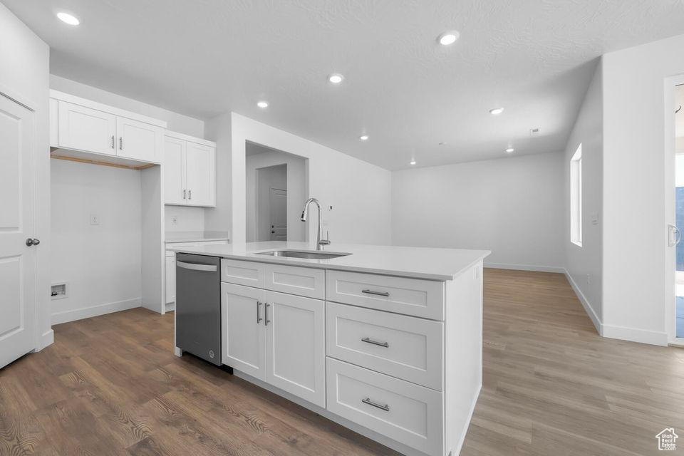 Kitchen with dishwasher, white cabinetry, light wood-style flooring, light countertops, and a kitchen island with sink