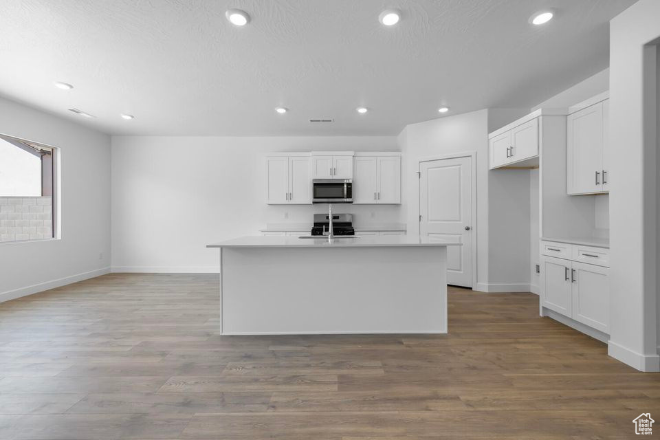 Kitchen featuring stainless steel microwave, white cabinets, range, and recessed lighting