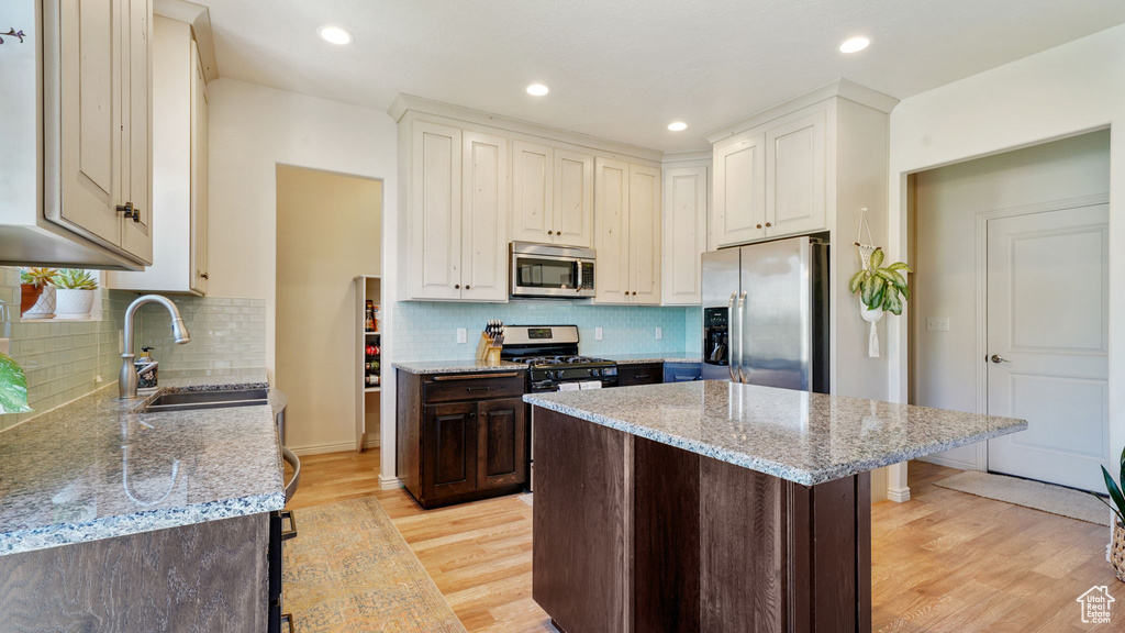 Kitchen with appliances with stainless steel finishes, light wood-style floors, a center island, light stone countertops, and backsplash