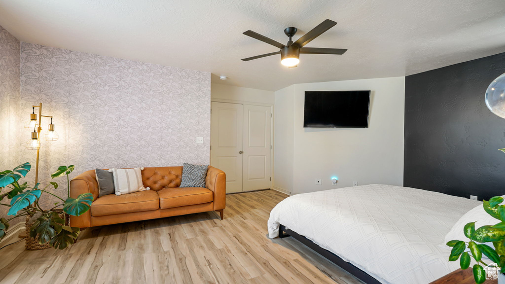 Bedroom with wallpapered walls, wood finished floors, and ceiling fan
