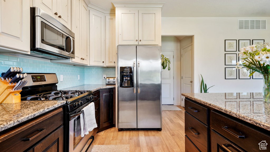 Kitchen with appliances with stainless steel finishes, light wood-type flooring, white cabinetry, dark brown cabinetry, and light stone countertops