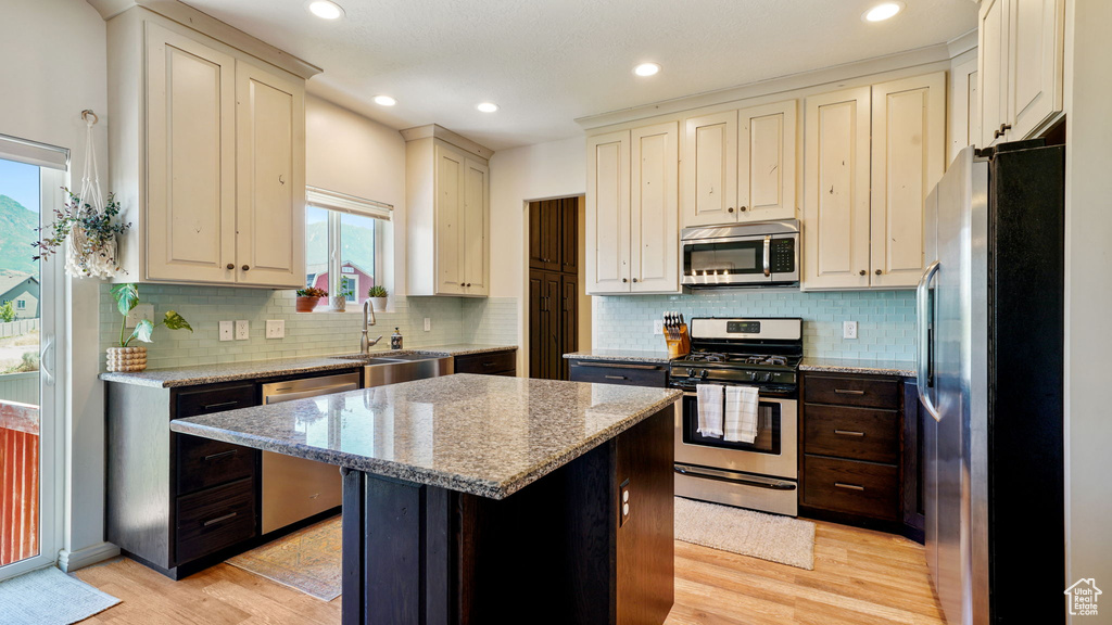 Kitchen with appliances with stainless steel finishes, light wood-style flooring, a kitchen island, light stone counters, and tasteful backsplash