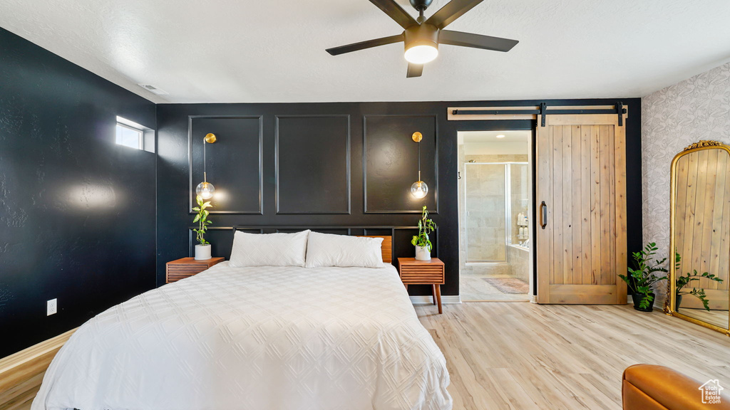 Bedroom with light wood-style flooring, wallpapered walls, a barn door, a ceiling fan, and ensuite bath