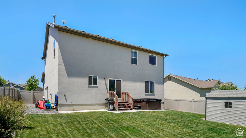 Back of house featuring a hot tub, a fenced backyard, stucco siding, and a storage shed