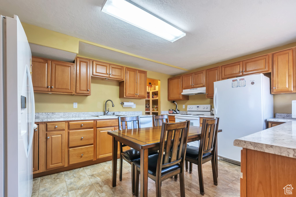 Kitchen with white appliances, under cabinet range hood, a textured ceiling, and brown cabinets
