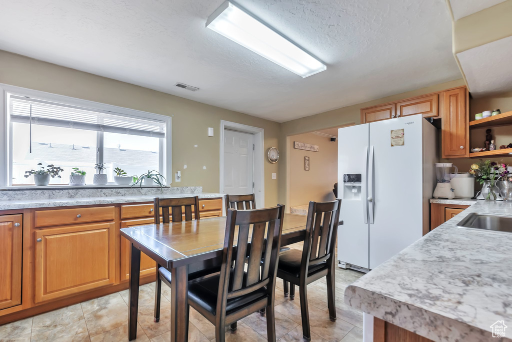Kitchen featuring white refrigerator with ice dispenser, light countertops, brown cabinets, open shelves, and a textured ceiling