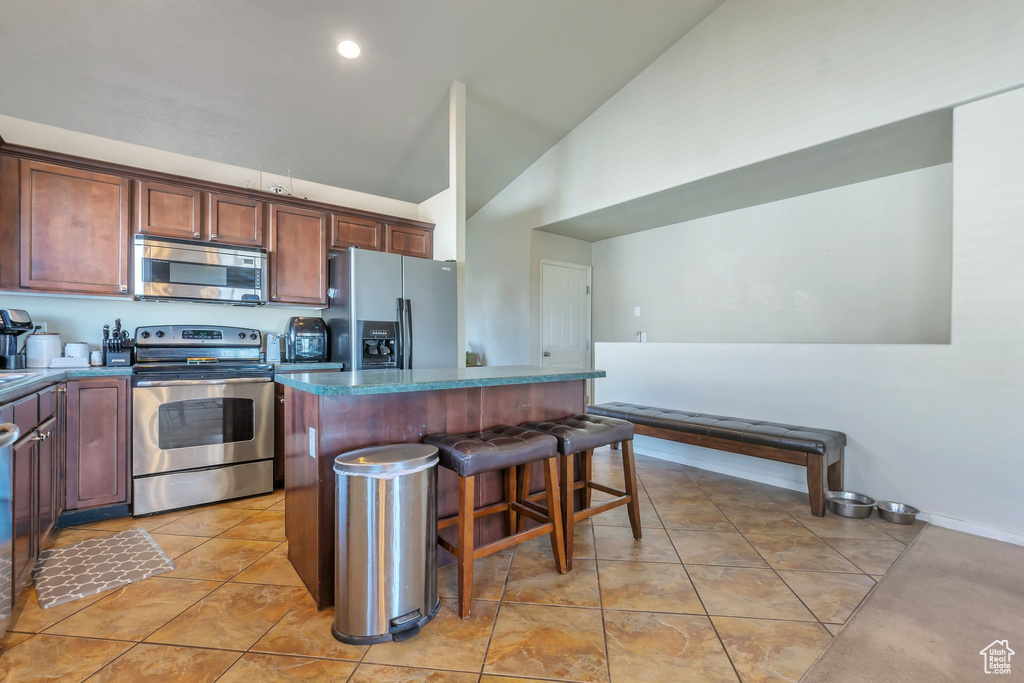 Kitchen featuring stainless steel appliances, a center island, a breakfast bar, high vaulted ceiling, and light tile patterned floors