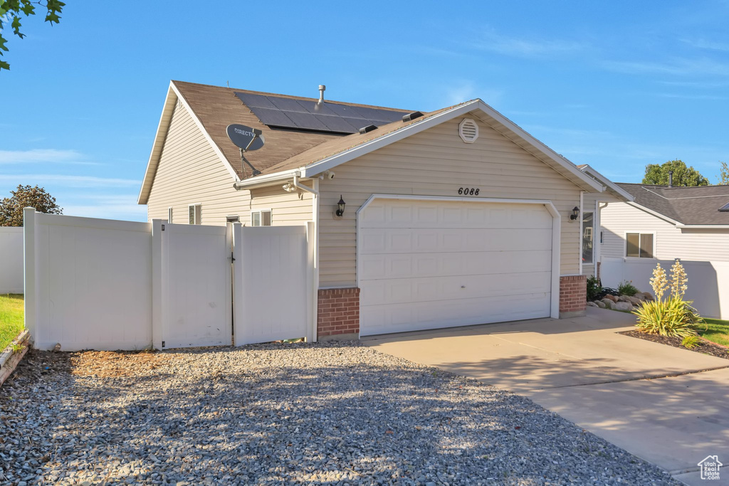 View of side of property with brick siding, concrete driveway, a garage, solar panels, and a shingled roof