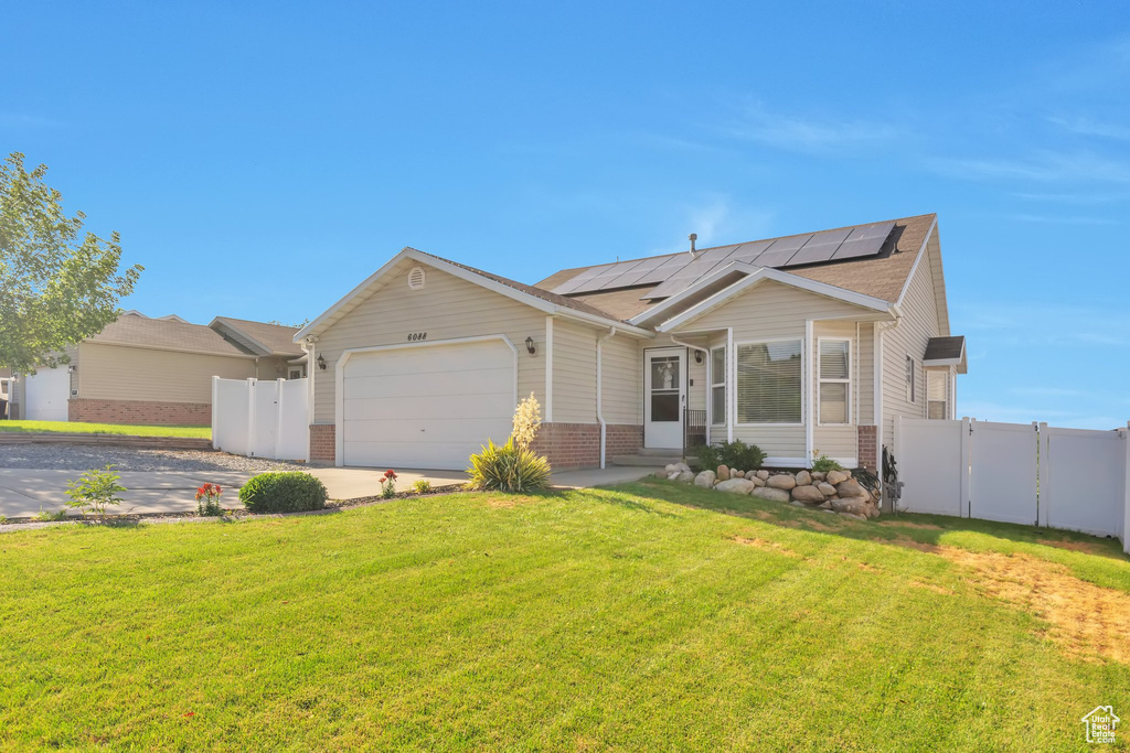 View of front facade featuring a gate, roof mounted solar panels, an attached garage, driveway, and brick siding