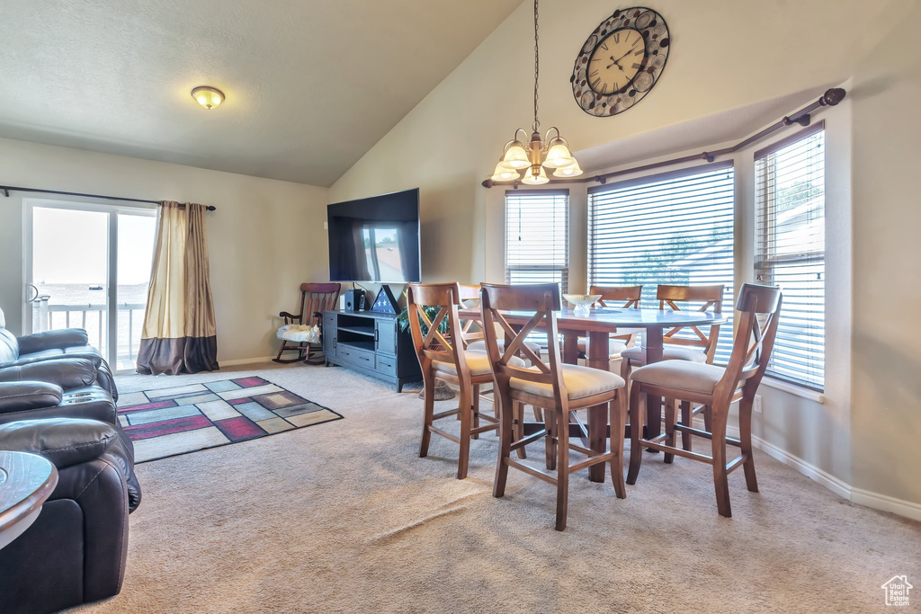 Carpeted dining space with a chandelier, healthy amount of natural light, and high vaulted ceiling