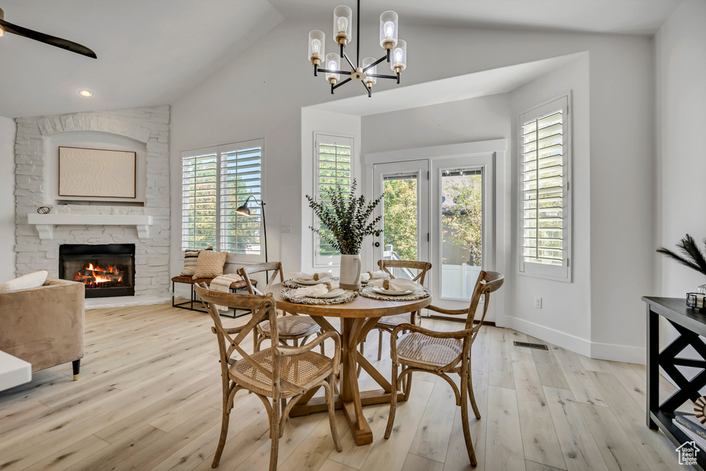 Dining area with lofted ceiling, light wood finished floors, a fireplace, a chandelier, and recessed lighting