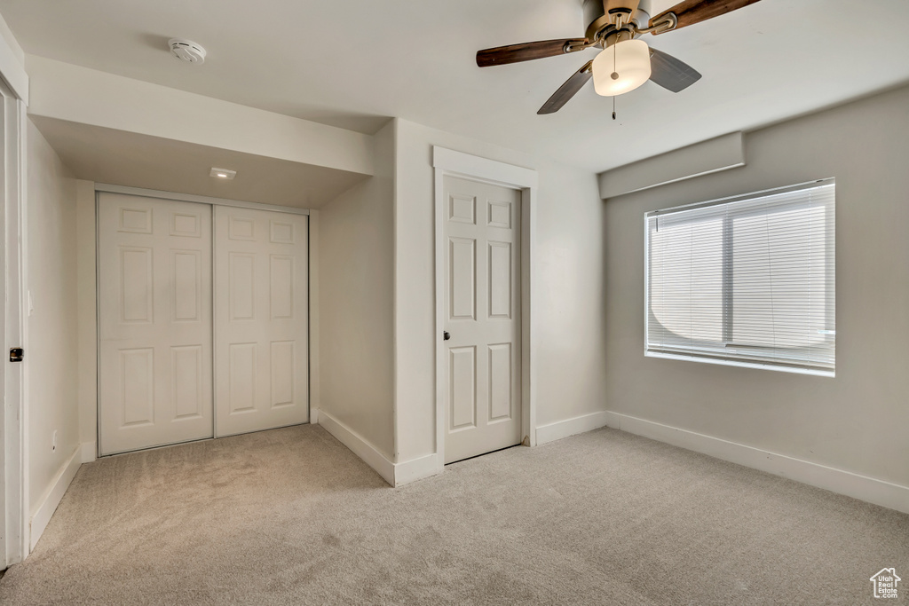 Unfurnished bedroom with light carpet, a closet, and a ceiling fan