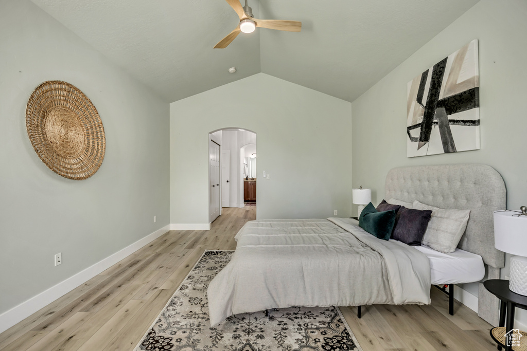 Bedroom with arched walkways, light wood finished floors, lofted ceiling, and a ceiling fan