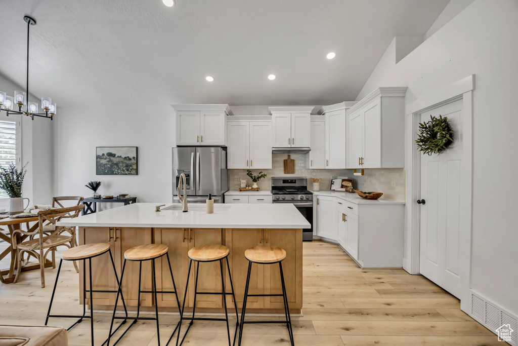 Kitchen featuring appliances with stainless steel finishes, an island with sink, a breakfast bar, backsplash, and light wood-style flooring
