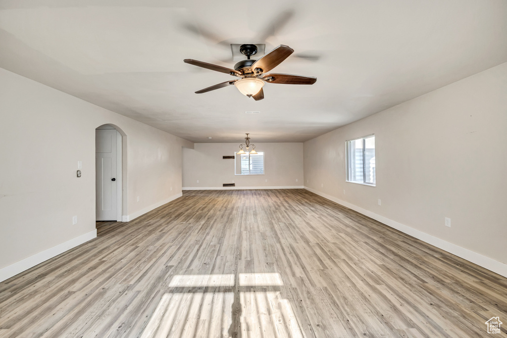 Unfurnished room with ceiling fan, light wood finished floors, arched walkways, and a chandelier