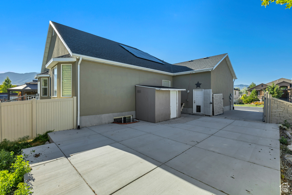 Back of house featuring solar panels, stucco siding, a patio area, a shingled roof, and a mountain view