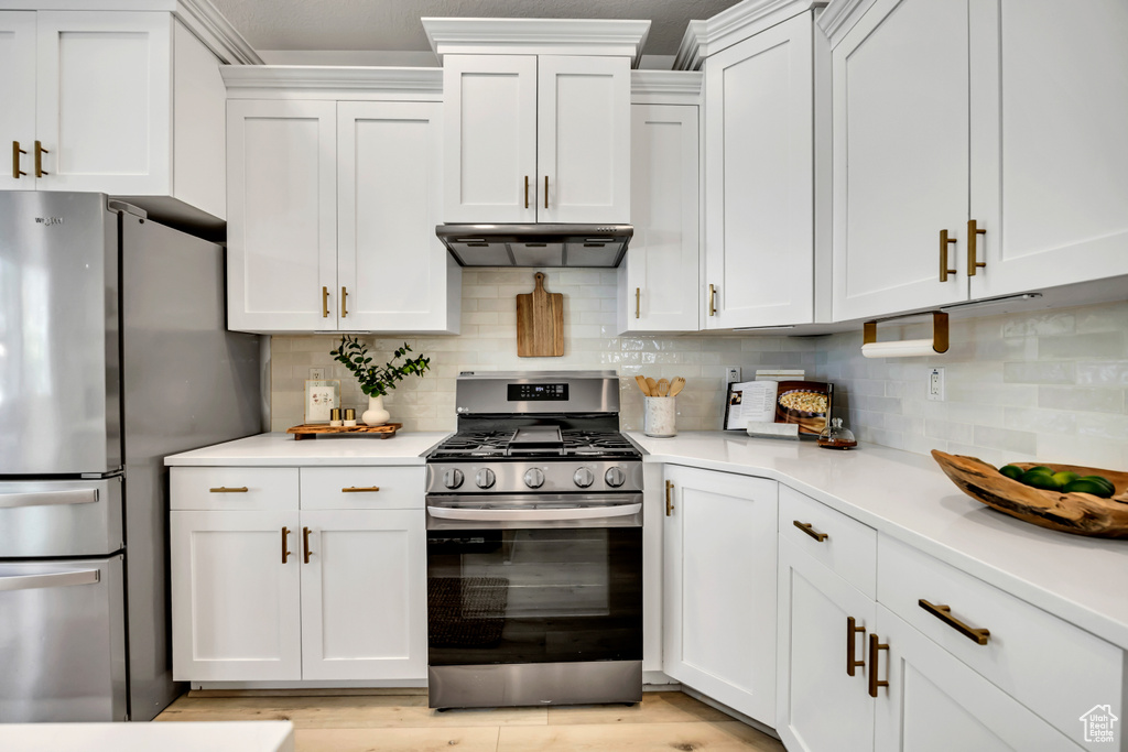 Kitchen with stainless steel appliances, light countertops, white cabinets, tasteful backsplash, and under cabinet range hood