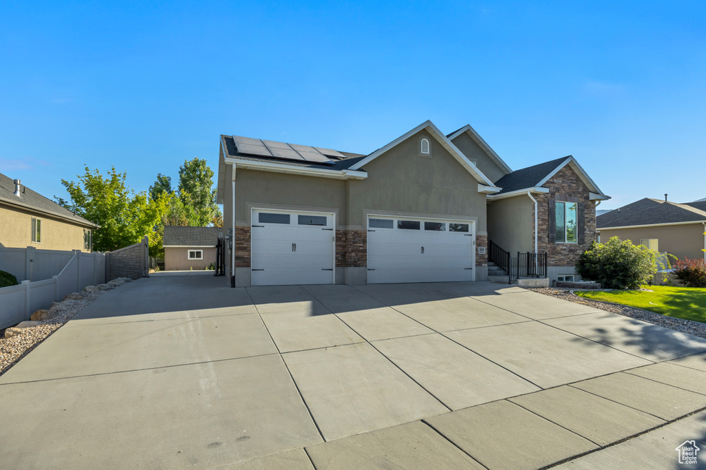 View of front of home featuring stone siding, stucco siding, roof mounted solar panels, driveway, and a garage