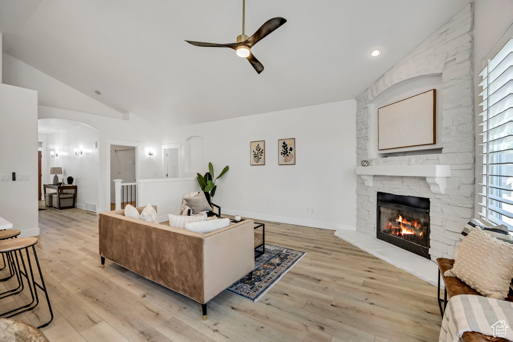 Living area featuring a ceiling fan, lofted ceiling, arched walkways, a fireplace, and light wood-type flooring