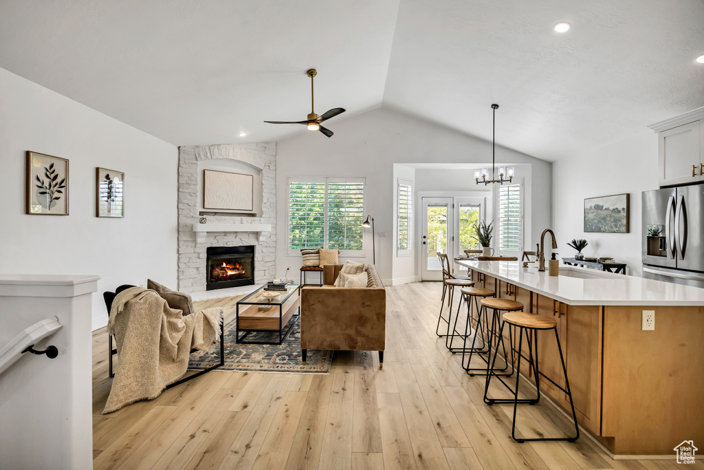Living room with ceiling fan, lofted ceiling, a fireplace, light wood-style flooring, and a chandelier