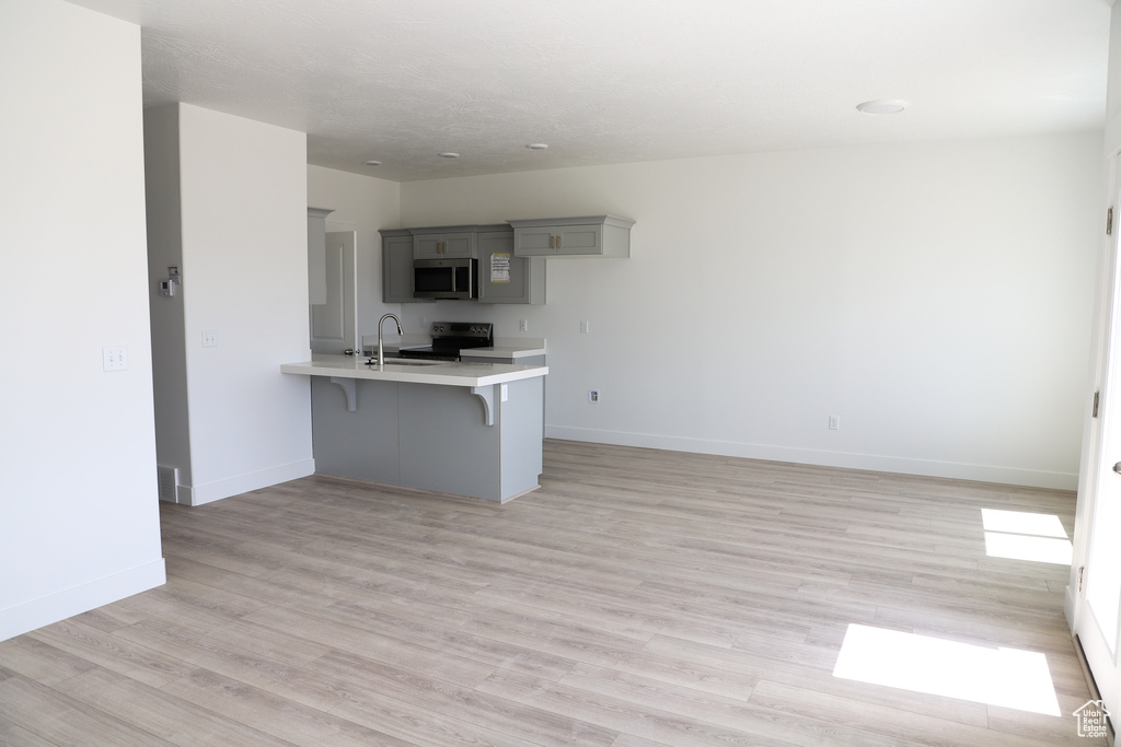 Kitchen featuring electric range, a peninsula, gray cabinets, a kitchen bar, and light countertops